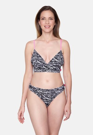 Femme portant un soutien-gorge imprimé zèbre noir et blanc avec des bretelles roses et un bas de bikini assorti, debout devant un fond clair uni.