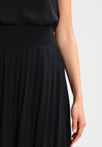 Musta liehitettävä hame, jossa on leveä, joustava vyötärö; sileä pinta; puolipitkä; virtaviivainen muotoilu; korostettu pystyraidoilla liikkumista varten.