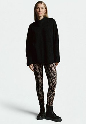 Schwarzer, übergroßer Strickpullover mit hohem Kragen, kombiniert mit Leggings im Leopardenmuster und schwarzen Schnürkampfstiefeln.