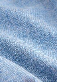 Közeli felvétel puha, világoskék szövött anyagról, amely finom textúrát és a anyagban enyhe redőket mutat.