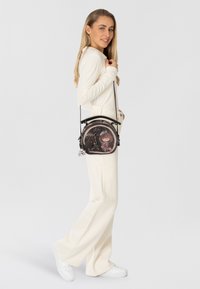 Borsa nera rotonda con illustrazioni colorate; texture liscia; tracolla regolabile; presenta design giocosi e dettagli hardware.
