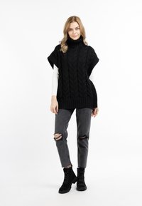 Schwarzer, gestrickter Poncho mit hohem Kragen und strukturiertem Muster, kombiniert mit grauen, gerissenen Jeans und schwarzen Schnürstiefeln.