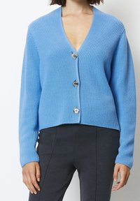 Ljusblå cardigan i ribbat stickat med V-hals, med tre stora runda knappar framtill och en kortad nederkant.