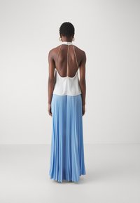 Haut halter blanc avec dos ouvert, mettant en avant un détail en chaîne dorée. Jupe plissée fluide en bleu clair, créant un effet superposé.