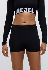 Mustad sportlikud lühikesed püksid, valmistatud siledast kangast, millel on keha järgiv lõige ja õmbluse detailid. Kandmisega sobib sama materjalist pikkade varrukatega särk.