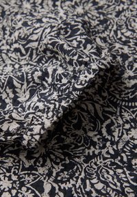 Tissu à motif floral bleu marine et crème avec une surface texturée, présentant des designs enroulés complexes et un drapé doux.