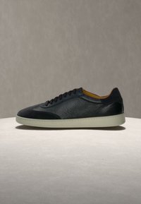Μαύρο δερμάτινο sneaker χαμηλού τύπου με μαύρα κορδόνια και λευκή σόλα, εμφανίζεται σε πλευρική προβολή σε ανοιχτή επιφάνεια με γκρι μονόχρωμο φόντο.