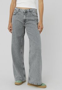 Jeans évasés en denim gris délavé avec un design classique à cinq poches, présentant une taille haute et des détails de décoloration subtile.