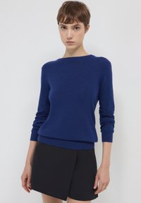 Blauer Pullover aus weichem Material, mit Rundhalsausschnitt und langen Ärmeln, kombiniert mit einem schwarzen Rock. Glatte Textur.