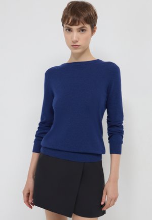 Maglione blu realizzato in materiale morbido, con collo rotondo e maniche lunghe, abbinato a una gonna nera. Texture liscia.