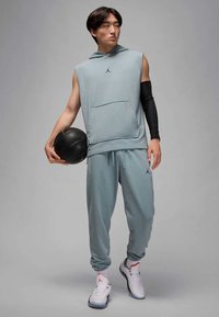 Svetlo modra brezrokavnik s kapuco in sprednjim žepom, kombiniran z ujemajočimi se ožjimi hlačami. Črna rokavica na roki in košarka. Bele športne čevlje z detajli.