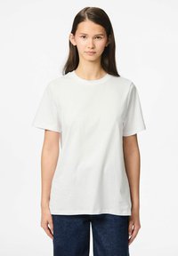 Vit bomull t-shirt med rund hals, korta ärmar och avslappnad passform. Slät textur och enkelt design, i kombination med mörkblå jeans.