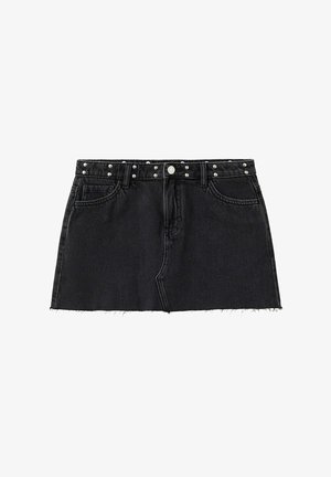 Jonge vrouw draagt een crèmekleurige gesmockte haltertop, een zwarte denim minirok, bruine sandalen met studs en draagt een zwarte schoudertas.