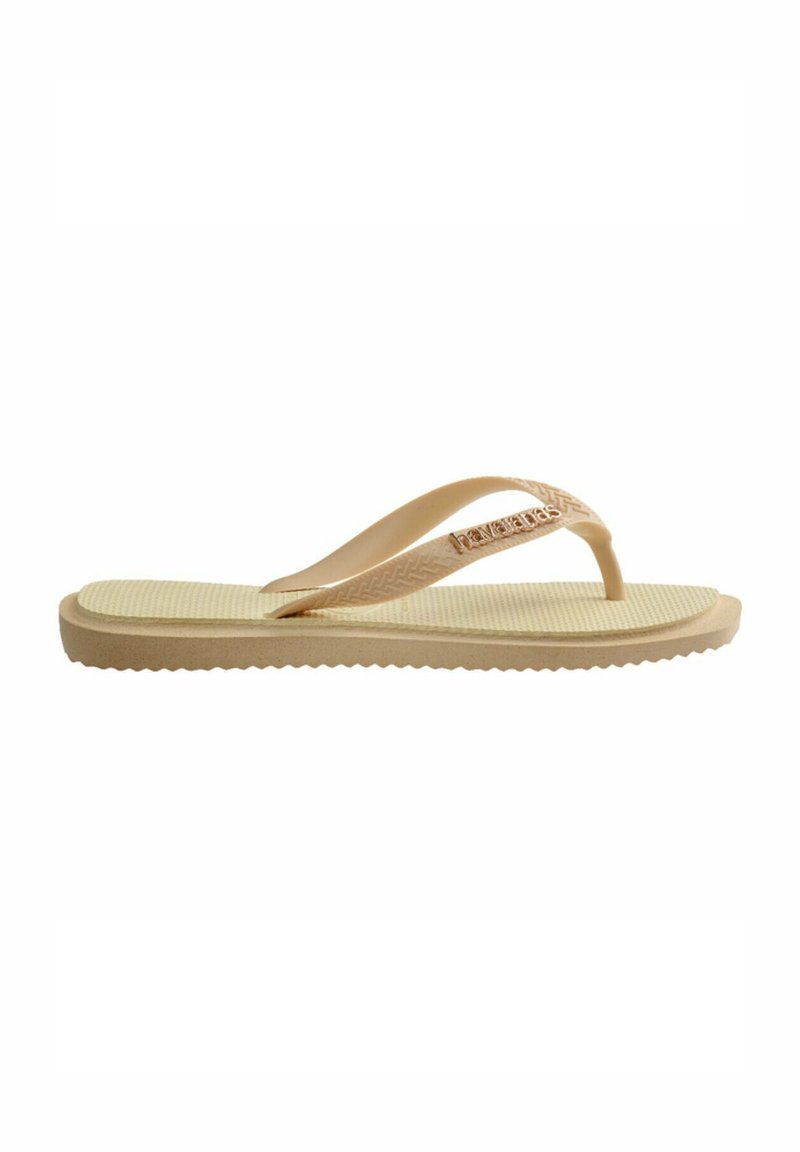 Sandale flip-flop tan avec semelle texturée, fines lanières et détail logo. Fabriquée en matériau flexible avec une semelle extérieure nervurée pour une meilleure adhérence.