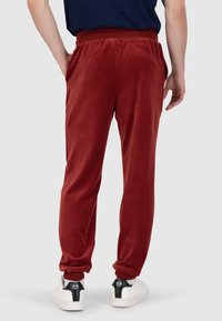 Rote Sweatpants aus weichem Stoff mit elastischem Bund, seitlichen Taschen und schmal zulaufenden Beinabschlüssen. Kombiniert mit weißen Sneakers.