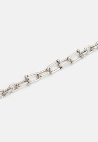 Corrente de metal prateado com elos alongados e bordas arredondadas, apresentando pequenos acessórios esféricos em toda a extensão, destacando uma superfície polida.