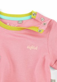 Różowa bawełniana koszula z okrągłym dekoltem, zdobiona żółtymi i turkusowymi prążkowanymi wykończeniami. Posiada zapięcia na zatrzaski i haftowane logo.