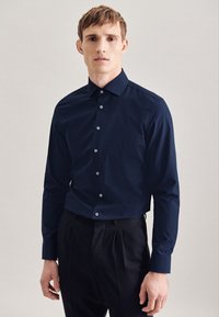 Camicia blu navy con bottoni, colletto a punta, maniche lunghe e tessuto strutturato. Presenta bottoni di colore chiaro lungo il davanti.