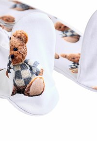 Weiße Socken mit einem Teddybaummotiv, mit strukturiertem braunem Fell und einem blau karierten Pullover, verziert mit einem weichen, glatten Stoff.