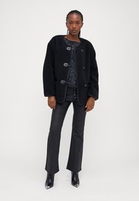 Čierna flisová bunda so zapínaním na gombíky, zaobleným golierom, štruktúrovaným povrchom, skombinovaná s priliehavými čiernymi nohavicami a špicatými čiernymi čižmami.