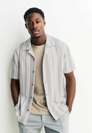 Kurzärmeliges Hemd mit Knopfleiste in Hellgrau mit vertikalen braunen Streifen, aus einem weichen Stoff, über einem beigen T-Shirt getragen. Legere Passform.