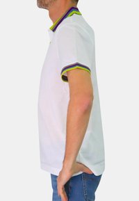 Polo bianco con colletto multicolore e dettagli dei polsini in viola, verde e grigio. Maniche corte, vestibilità casual, texture liscia.