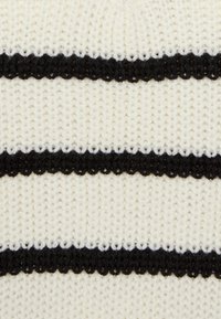 Tissu tricoté crème avec des rayures noires horizontales. Texture douce avec des détails de couture visibles. Chaque rayure a un bord ondulé.