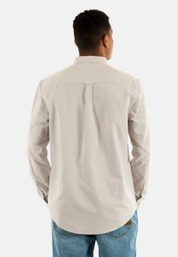 Camicia a maniche lunghe color beige chiaro con colletto in bottoni, design con yoke e piega sul retro, abbinata a jeans blu chiaro. Tessuto con texture liscia.