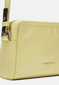 Borsa a tracolla gialla in pelle con chiusura a zip, tracolla nera regolabile e logo del marchio impresso di lato, con dettagli di cucitura ordinati.