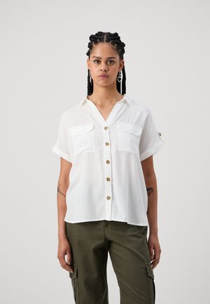 Blusa bianca a maniche corte con abbottonatura frontale, due tasche sul petto e maniche arrotolate, realizzata in tessuto leggero.