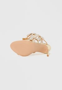 Kuldne sandaal kaunite litritega lillemustriga, avatud kontsaga ja tekstuuriga tallaga. Omab madalat ja peent kontsa.