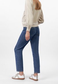 Beige svetr s bílými pruhy, modré rovné džíny a světle šedé tenisky. Volný střih, měkká textura a jednoduchý design.