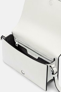 Biała skórzana torebka crossbody o gładkiej fakturze, z zatrzaskiem magnetycznym, wewnętrzną kieszenią na zamek i regulowanym paskiem. Czarna podszewka z detalem marki.