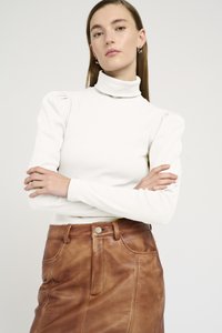 Haut col roulé blanc à côtes avec des manches bouffantes, associé à une jupe en cuir marron avec des poches avant et un détail de bouton en métal.