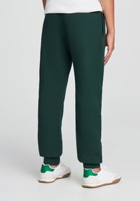 Ciemnozielone spodnie dresowe o zwężanym kroju, z elastycznymi mankietami i kieszeniami bocznymi, połączone z białymi trampkami z zielonymi akcentami.