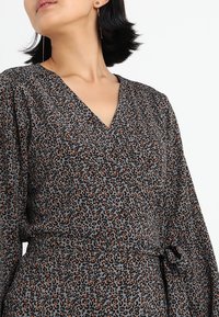 Robe à motif léopard en gris, avec un décolleté en V, des manches longues, une taille cintrée avec une ceinture et un tissu doux et texturé.