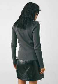 Szürke bordázott, hosszú ujjú felső fekete fényes mini szoknyával párosítva. Az öltözet texturált anyagot kombinál egy sima, fényes felszínnel.