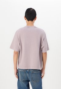 Short-sleeve, pastel purple t-shirt with a crew neck, relaxed fit, and minimal stitching detail, paired with blue denim jeans.