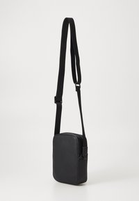 Borsa a tracolla nera in pelle vegana con forma rettangolare, tracolla regolabile e cerniere senza cuciture per una conservazione sicura. Finitura a texture liscia.