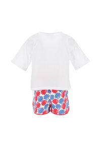 T-shirt bianco a maniche corte abbinato a pantaloni da mare blu e rossi con motivi a conchiglia e orlo scallop.