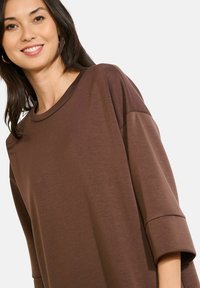Braunes übergroßes Oberteil mit rundem Ausschnitt und kurzen Ärmeln. Weicher Stoff mit glatter Textur, das einen lockeren Sitz bietet.