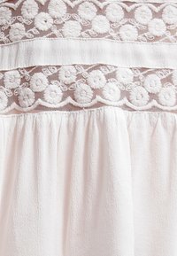 Tissu blanc avec broderie florale texturée et panneaux de maille transparente au-dessus d'un tissu plissé froncé en dessous.