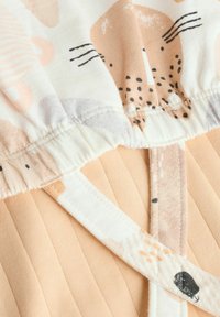 Vêtement en tissu présentant un haut doux crème avec des motifs animaliers abstraits en pêche et gris, associé à un bas texturé pêche et des bretelles réglables.