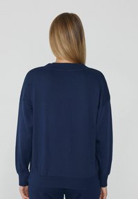 Sudadera azul marino con un corte relajado, mangas largas y puños acanalados. Cuenta con cuello redondo y una textura de tela suave y lisa.