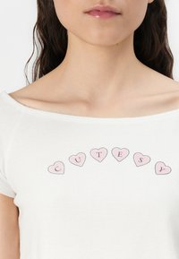 Baltos off-shoulder marškinėliai pagaminti iš medvilnės; puošti spalvingais širdelės formos raštais su tekstu "CUTESY" centre. Minkšta tekstūra.