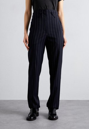 Navy pinstriped trousers with a high waist and pleated design. Made of a smooth fabric. Paired with glossy black shoes.