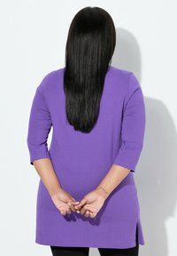Fioletowa tunika z rękawami do łokcia, o prostym kroju i bocznych rozcięciach, wykonana z gładkiej, miękkiej tkaniny.