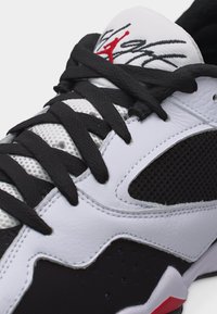 Λευκό και μαύρο αθλητικό παπούτσι με μαύρα κορδόνια, λεπτομέρειες από δίχτυ και γλώσσα με κόκκινο λογότυπο Jumpman και υπογραφή.