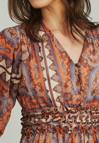 Leuchtend orange- und cremefarbenes Kleid mit komplizierten Paisleymustern, rüschigem elastischen Bund und V-Ausschnitt mit Knopfdetails.