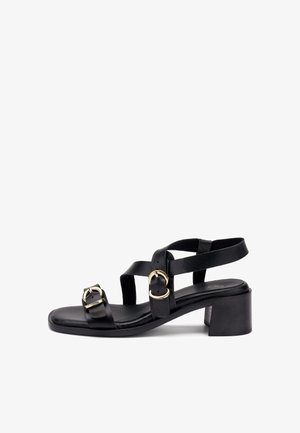 Sandalia de cuero negro con tacón bajo de bloque, con dos correas con hebillas doradas y diseño de punta abierta.
